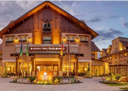 Wyndham Gramado Termas Resort & Spa Ngoại thất bức ảnh The photo shows a charming lodge or hotel building with a wooden exterior, characterized by a sloping roof and multiple windows. The entrance is well-lit and features a sign that appears to identify the establishment. There are several flags displaye