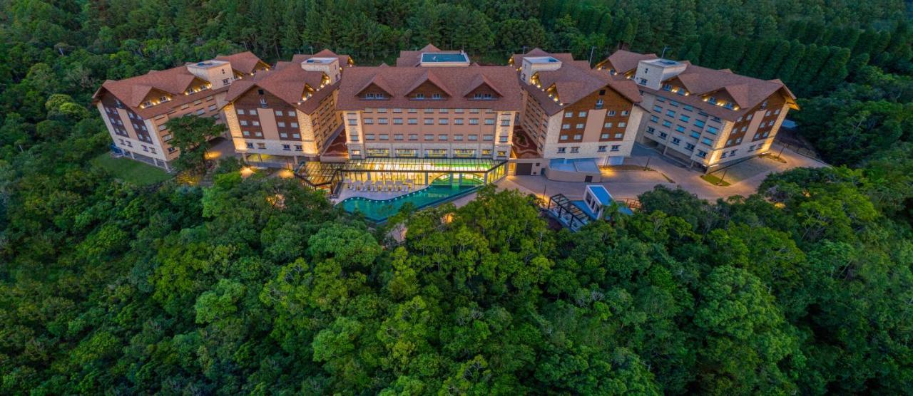 Wyndham Gramado Termas Resort & Spa Ngoại thất bức ảnh The photo shows a resort or hotel complex surrounded by lush greenery. The buildings have a modern design with multiple stories, featuring a mix of large windows and distinctive roofs. There is a swimming pool area visible, which appears to be integr
