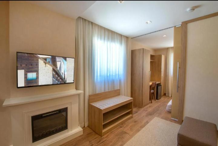 Wyndham Gramado Termas Resort & Spa Ngoại thất bức ảnh The photo shows a modern interior of a room. On one side, there is a flat-screen TV mounted on the wall above a stylish fireplace with a white mantel. In front of the TV, there is a wooden bench, which has a simple design. The room has large windows 