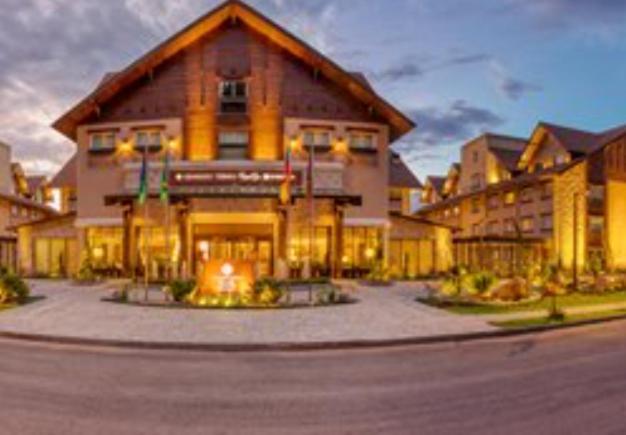 Wyndham Gramado Termas Resort & Spa Ngoại thất bức ảnh The photo shows an exterior view of a lodge or hotel, designed in a rustic style with wooden accents. The building features a gable roof, large windows, and well-lit entrance, suggesting a warm and welcoming atmosphere. The landscape around it includ