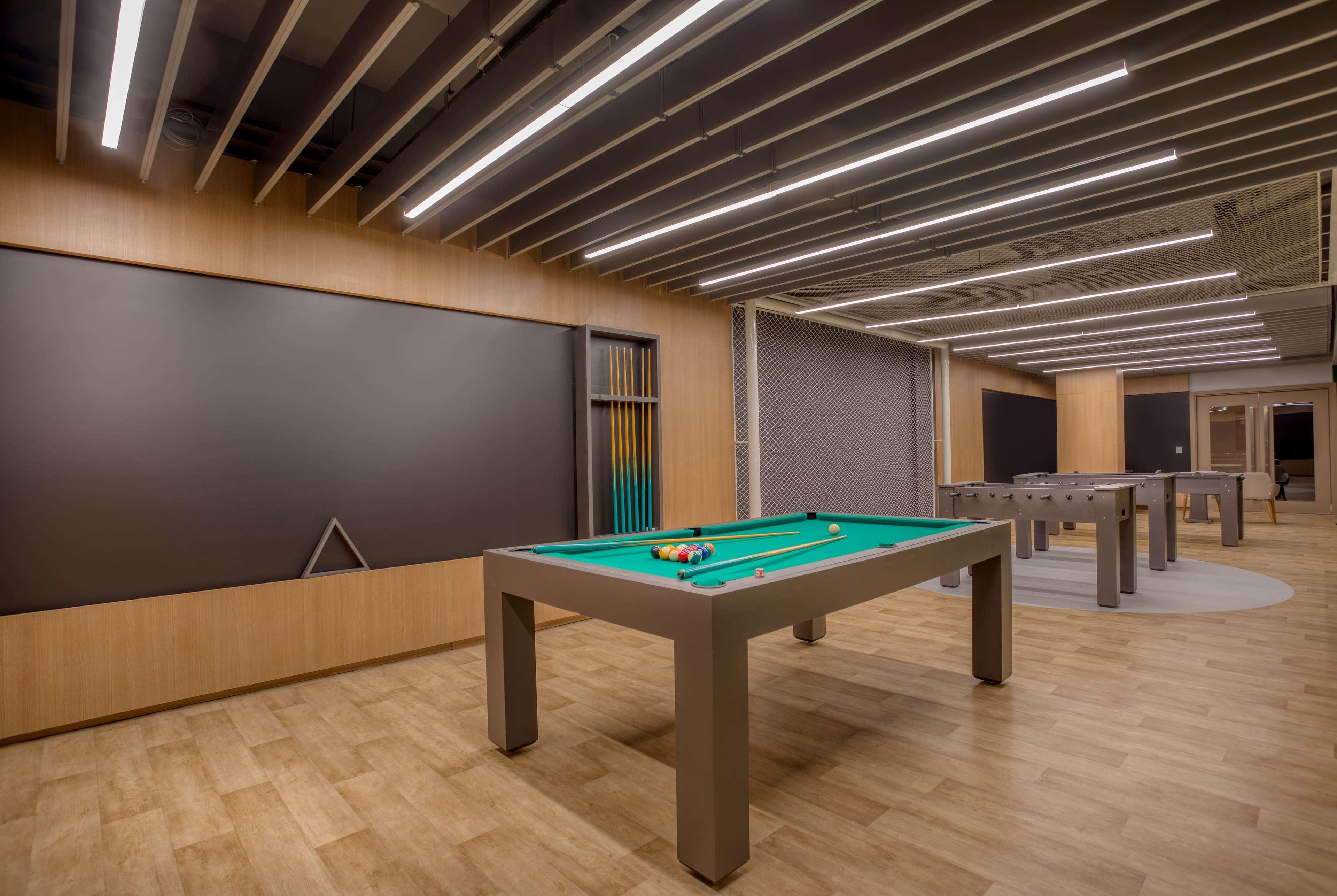 Wyndham Gramado Termas Resort & Spa Ngoại thất bức ảnh The photo shows a modern recreational room featuring several pool tables. In the center, there is a green felt pool table with balls arranged on it. The room has wooden flooring and is illuminated by overhead lights with a sleek design. The walls are