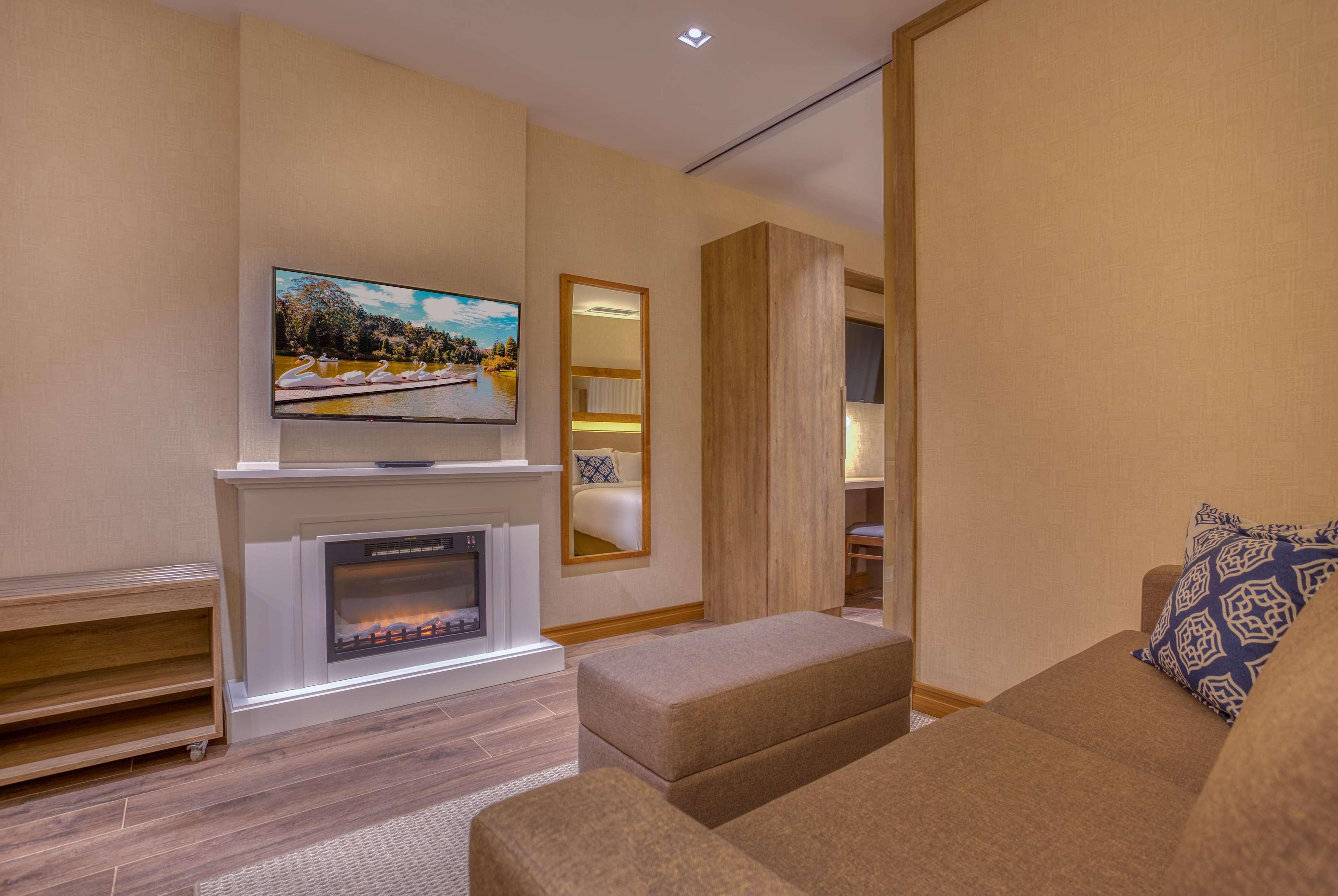 Wyndham Gramado Termas Resort & Spa Ngoại thất bức ảnh The photo shows a cozy living space featuring a comfortable sofa, a modern television mounted on the wall, and a stylish electric fireplace beneath it. There is a decorative element on the wall, possibly a small shelf or cabinet. The room is well-lit