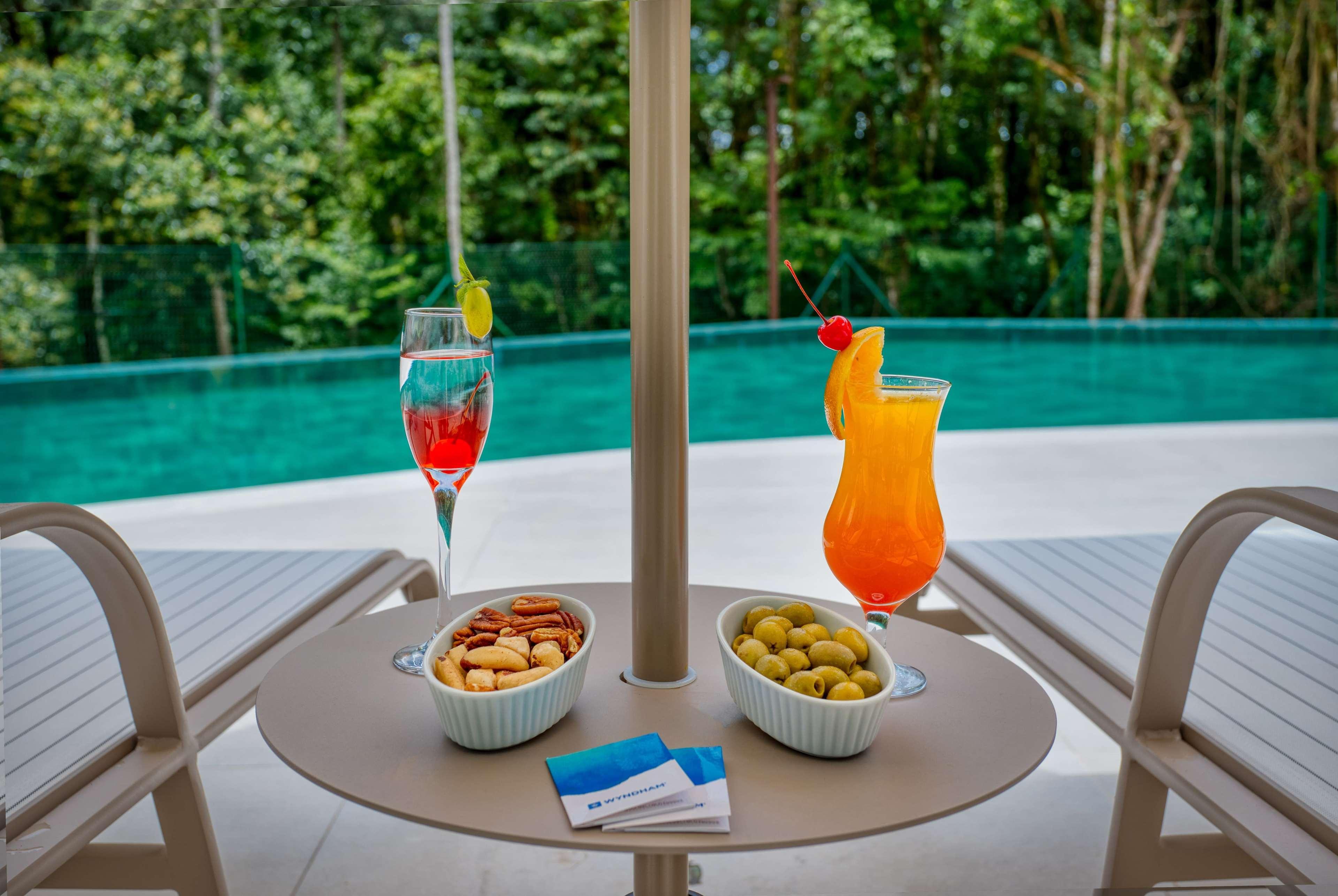 Wyndham Gramado Termas Resort & Spa Ngoại thất bức ảnh The photo shows a table on a patio or by a poolside with two vibrant cocktails. One is a pink drink with a lemon slice, and the other is an orange drink garnished with a cherry and an orange slice. There are also two small bowls: one containing mixed