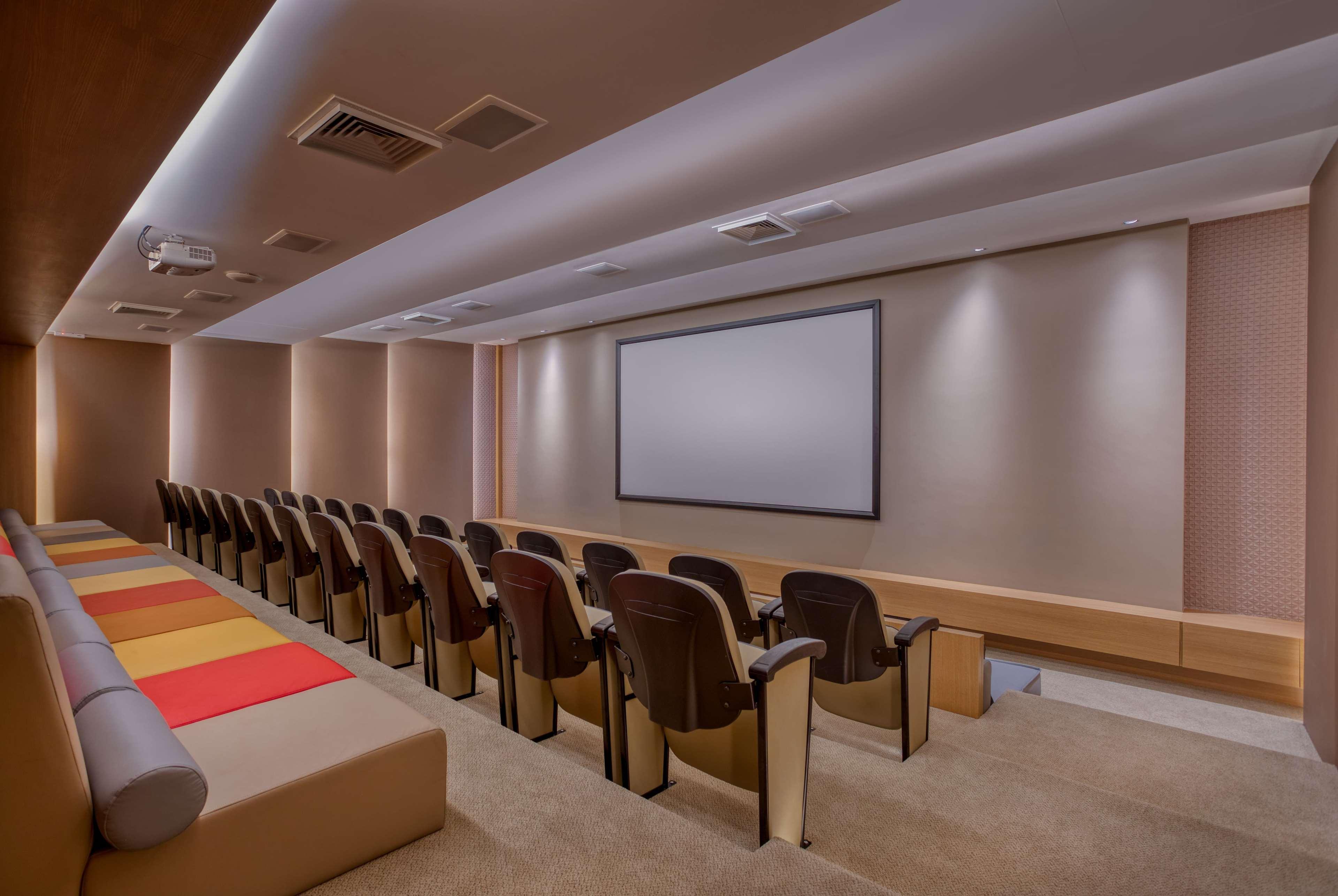 Wyndham Gramado Termas Resort & Spa Ngoại thất bức ảnh The image shows a modern and elegantly designed home theater or screening room. It features a row of brown armchairs arranged in a semi-circle facing a large, blank projection screen mounted on the wall. The room has neutral-colored walls with soft l