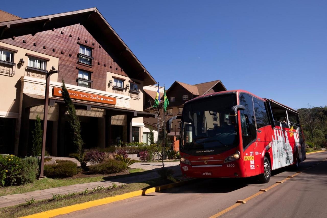 Wyndham Gramado Termas Resort & Spa Ngoại thất bức ảnh The photo shows a red bus parked in front of a large building, which appears to be a hotel or lodge. The building features a rustic architectural style, with wooden elements and large windows. There are trees and landscaping around the entrance, and 