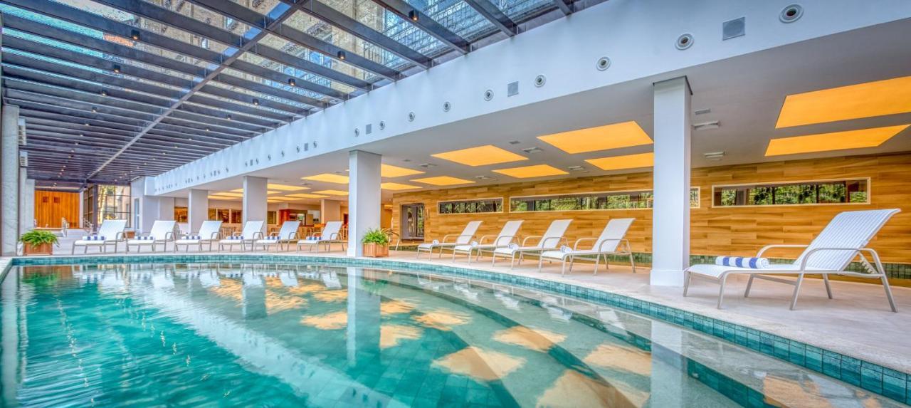 Wyndham Gramado Termas Resort & Spa Ngoại thất bức ảnh The photo shows an indoor swimming pool area. The pool is surrounded by light-colored walls, and there are several white lounge chairs neatly arranged beside it. The ceiling features a modern design with beams and glass panels, allowing natural light